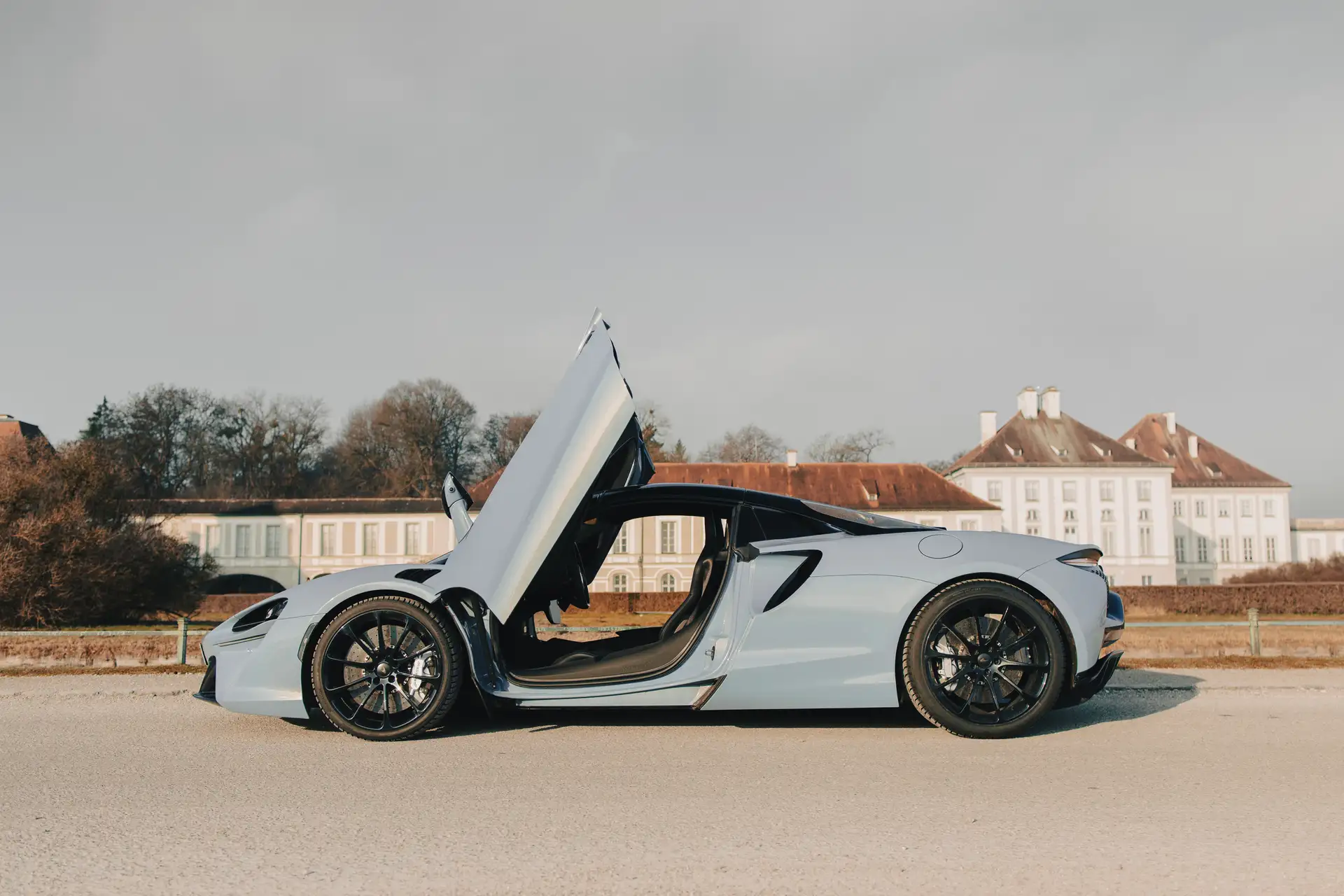 McLaren Atura Spider mit geöffneten Flügeltüren steht seitlich auf einem Platz vor einem großen historischen Gebäude